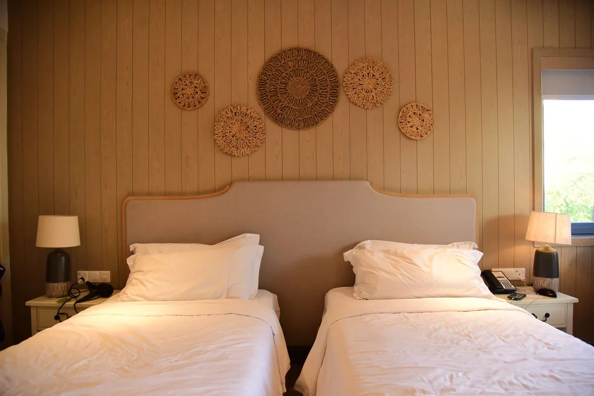A two-bed non-air-conditioned room with a warm wooden headboard wall